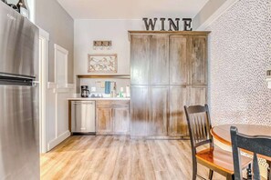 A kitchen with a stainless steel refrigerator, a wooden cabinet with 'WINE' on top, a coffee maker, and a dining table with chairs. - Updated Studio Oregon Wine Country - Kitchenette (McMinnville)