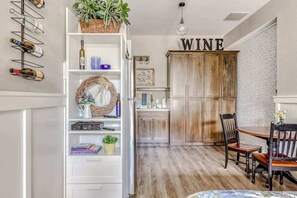 A dining area with a wooden table and chairs, a white shelving unit with wine bottles, and a cabinet labeled 'WINE'. - Updated Studio Oregon Wine Country - Kitchenette (McMinnville)
