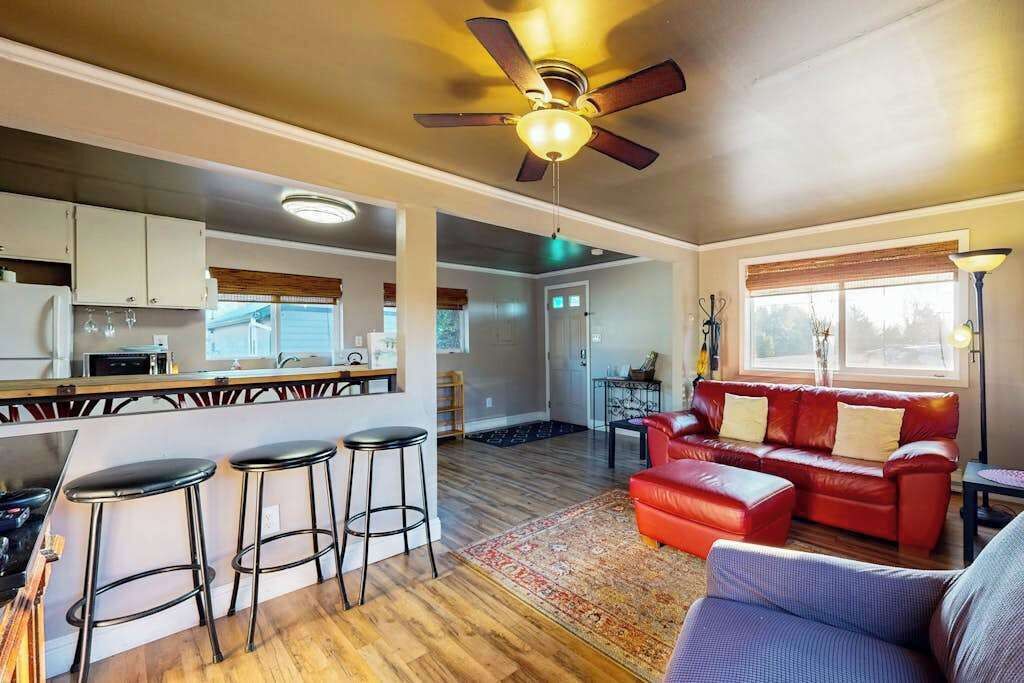 Amplia sala de estar con un sofá de cuero rojo, un sillón azul y una zona de cocina con un taburete de bar.