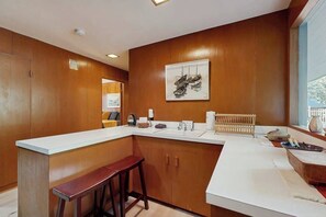 A modern kitchen with wooden cabinets, a white countertop, and a bar stool. - 1BR Apartment - Washer & Dryer - Dog-Friendly (Portland)