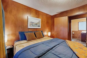 A hotel room with a wooden wall, a bed with blue and brown bedding, a framed picture on the wall, and a door leading to a bathroom. - 1BR Apartment - Washer & Dryer - Dog-Friendly (Portland)