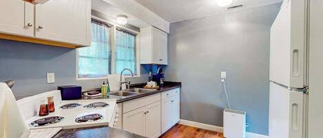 A compact kitchen with white cabinets, a gas stove, a sink, and a small refrigerator.