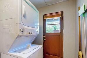 A laundry area with a washing machine, a door, and a broom leaning against the wall. - 2BR peaceful getaway with patio & W&D - near river (Milwaukie)
