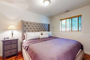 A bedroom with a tufted headboard, a bed with a purple bedspread, a bedside table with a lamp, and a window with blinds. - 2BR peaceful getaway with patio & W&D - near river (Milwaukie)