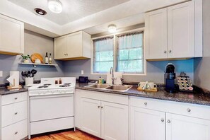 A kitchen with white cabinets, a stove, a sink, and a window with curtains. - 2BR peaceful getaway with patio & W&D - near river (Milwaukie)