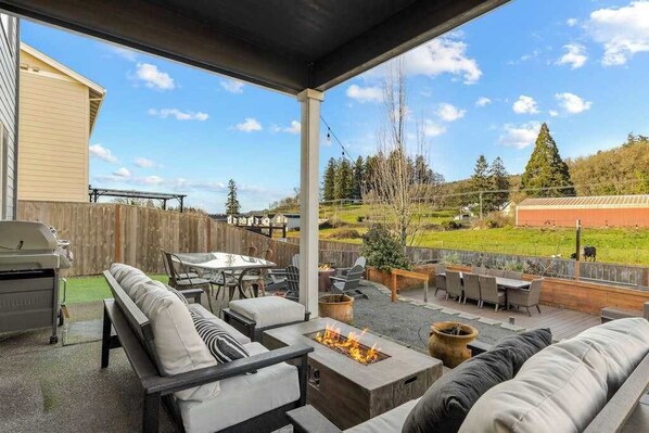 A covered outdoor patio with a fire pit, seating area, and a view of a grassy yard.