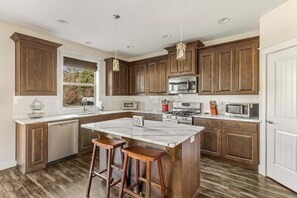 Eine moderne Küche mit Holzausbau, einer zentralen Kochinsel, Barhocker und Edelstahlgeräten.