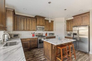 A modern kitchen with wooden cabinets, stainless steel appliances, and a marble island. - 5BR House - Fire Pit - Gas Grill - Washer & Dryer (Newberg)