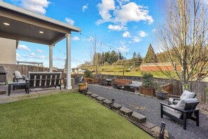A backyard with a covered patio, outdoor seating, and a landscaped garden. - 5BR House - Fire Pit - Gas Grill - Washer & Dryer (Newberg)