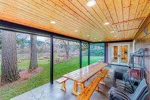 An outdoor dining area with a wooden table and benches, surrounded by glass walls and a view of a natural landscape. - 3BR river-view with deck, grill, & firepit (Milwaukie)
