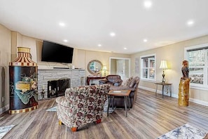 A living room with a fireplace, a television, and a large window. - 3BR river-view with deck, grill, & firepit (Milwaukie)