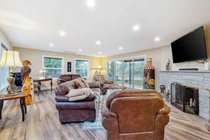 A spacious living room with a fireplace, leather sofas, and a flat-screen TV. - 3BR river-view with deck, grill, & firepit (Milwaukie)