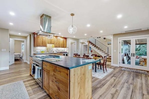 A modern kitchen with wooden cabinets, a central island, and a staircase leading to another level. - 3BR river-view with deck, grill, & firepit (Milwaukie)