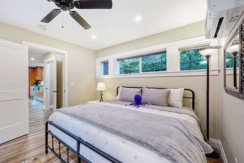 A bedroom with a bed, a ceiling fan, a window, and a lamp.