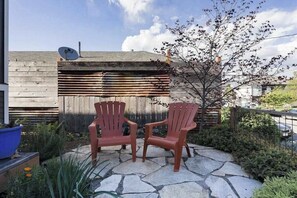 Two Adirondack chairs on a stone patio with a wooden fence and a tree in the background. - Blue Door Micro-Loft in Hip and Arty Location (Portland)