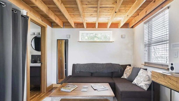 En moderne stue med træloft, sofa, sofabord og et vindue med persienner.