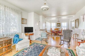 A spacious living room with a television, a dining area with a table and chairs, and a large window with curtains. - Historic 4BR Valleyview Oregon Wine Country DogsOK (McMinnville)