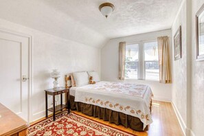 Ein Schlafzimmer mit einem Bett, einem Nachttisch, einem Fenster mit Vorhängen und einer Tür.