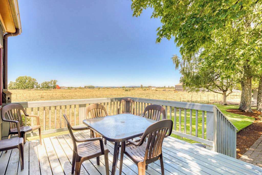 Eine Holzterrasse mit Tisch und Stühlen, mit Blick auf ein grasbewachsenes Feld und einen klaren Himmel.