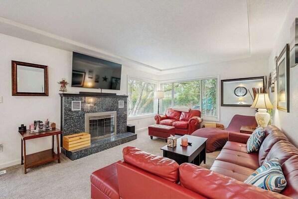 A living room with a fireplace, leather sofas, a coffee table, and a TV mounted on the wall.