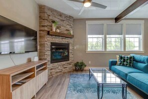 A living room with a stone fireplace, a flat-screen TV mounted on the wall, a blue sofa, and a glass coffee table. - High-End Studio Oregon Wine Country (McMinnville)