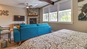 A room with a bed, a blue sofa, a fireplace, a television, and a window with blinds. - High-End Studio Oregon Wine Country (McMinnville)