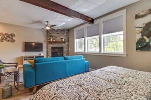 A room with a bed, a blue sofa, a fireplace, a television, and a window with blinds. - High-End Studio Oregon Wine Country (McMinnville)