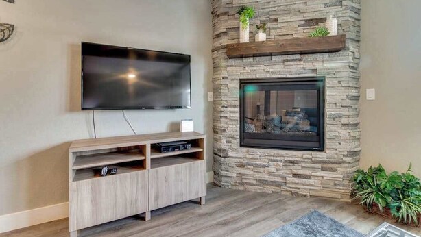 A living room with a flat-screen TV mounted on the wall, a wooden entertainment unit below, and a stone fireplace with a glass door. - High-End Studio Oregon Wine Country (McMinnville)