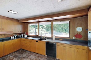 A kitchen with wooden cabinets, a black dishwasher, and a window with a view of greenery. - 3BR home with pool, patio, fireplace, WIFI (Portland)