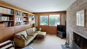 A living room with a sofa, a fireplace, a television, and bookshelves. - 3BR home with pool, patio, fireplace, WIFI (Portland)