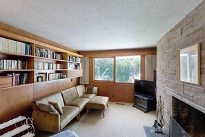 Ein Wohnzimmer mit einer Couch, einem Kamin, einem Fernseher und Bücherregalen.