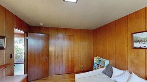 A bedroom with wooden paneling, a bed with pillows, a nightstand, and a window. - 3BR home with pool, patio, fireplace, WIFI (Portland)