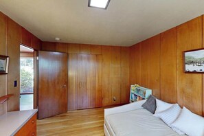 Ein Schlafzimmer mit Holzvertäfelung, einem Bett mit Kissen, einem Nachttisch und einem Fenster.