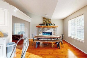 A spacious room with a wooden floor, a fireplace with a stone surround, and a dining table with chairs. - 3BR Oregon Wine Country - Fireplace - Patio (McMinnville)