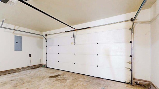 Een garage met een witte deur, een betonnen vloer en een zichtbaar stopcontact.