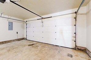 Un garaje con puerta blanca, suelo de concreto y un enchufe visible.