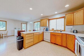 A modern kitchen with wooden cabinets, a dishwasher, and a large window. - Custom-built 2BR with deck & massage chairs (Gresham)