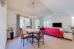 Ein Wohnzimmer mit rundem Tisch, Stühlen, einem roten Sofa, einem Flachbildfernseher und einer Topfpflanze.
