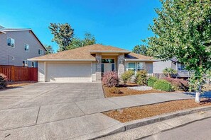 A residential house with a garage, a driveway, and a landscaped front yard with shrubs and a small tree. - Custom-built 2BR with deck & massage chairs (Gresham)