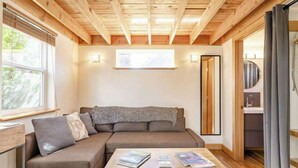 A cozy room with a wooden ceiling, a sofa, a coffee table with magazines, and a window. - Micro-Loft Surrounded by Gardens in Hip Location (Portland)