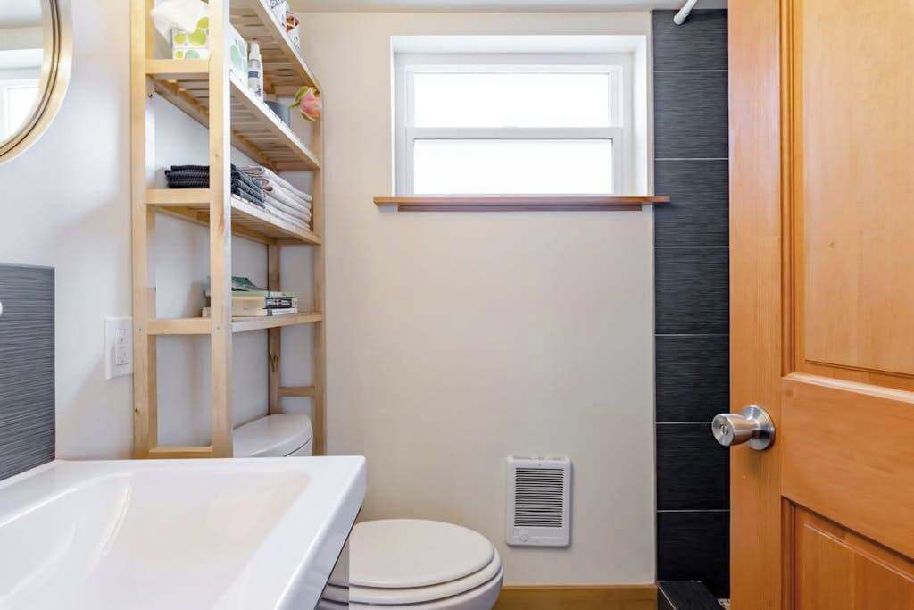 Une salle de bain comprenant des toilettes, une étagère, une fenêtre et une porte.