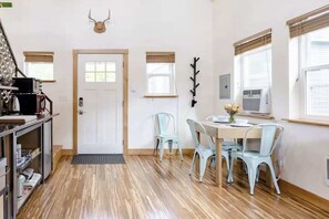 A room with a wooden floor, a white door, a dining table with four chairs, and a wall-mounted air conditioning unit. - Micro-Loft Surrounded by Gardens in Hip Location (Portland)