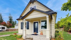 Uma casa térrea com varanda frontal, porta de cor escura e um pequeno jardim com plantas e um objeto decorativo.