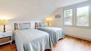 Quarto com duas camas, uma mesa de cabeceira com abajur e uma janela grande.