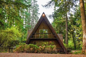 Eine Holzhütte mit Satteldach, einem Balkon und großen Fenstern, umgeben von dichtem Wald.