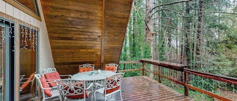 A wooden deck with a table and chairs, surrounded by a forest.