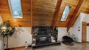A room with a stone fireplace, wooden ceiling beams, and skylights. - 2BR cabin with loft in wooded setting with WiFi (Beaverton)
