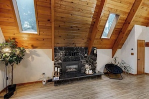Ein Zimmer mit Kamin aus Stein, Holzbalkendecke und Dachfenstern.