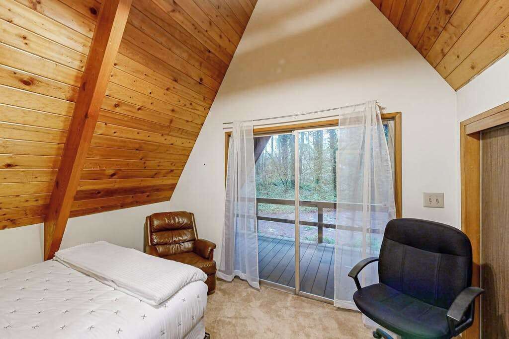 Een kamer met een schuine kap, een bed, een stoel en een raam met uitzicht op een terras.