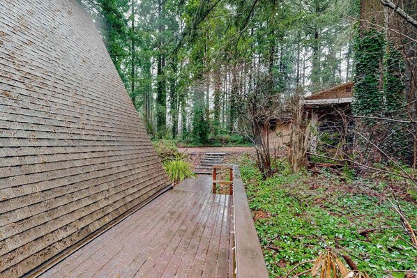 A wooden deck leading to a building with a sloped roof, surrounded by dense greenery and trees. - 2BR cabin with loft in wooded setting with WiFi (Beaverton)